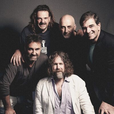 Five members of Hothouse Flowers huddled in a group, all smiling, wearing dark clothing