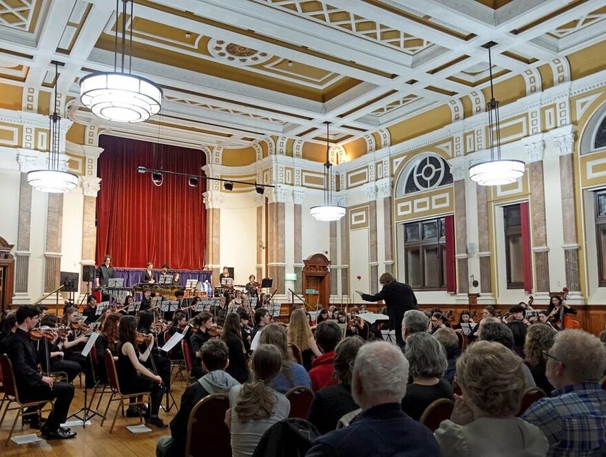 A town call with a youth orchestra playing and an audience facing them