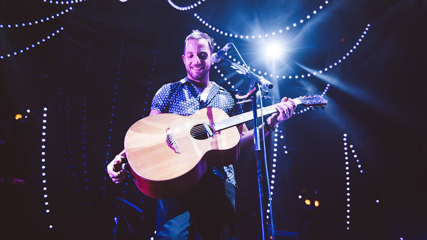 James Morrison with a guitar, on stage at Roundhouse, surrounded by hanging fairy-style lights