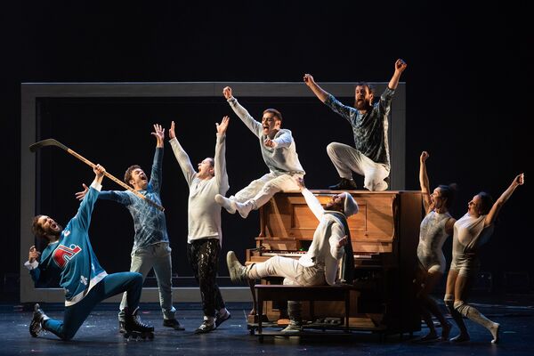 A group of performers posed around a piano, all with their hands in the air