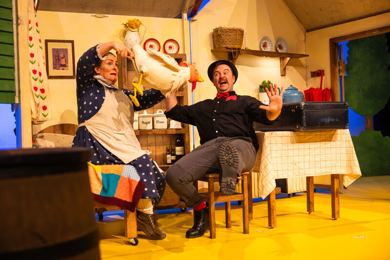A man sits down and looks shocked as a chicken puppet launches towards him, controlled by a woman