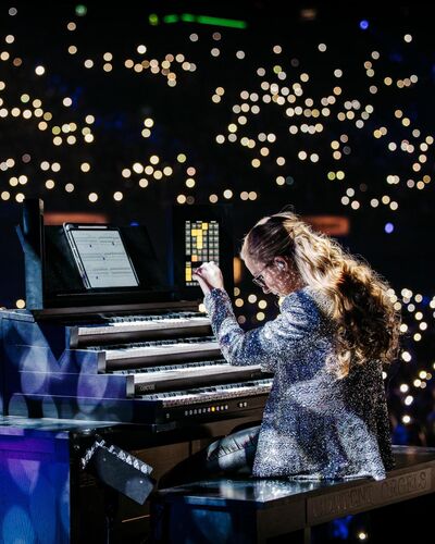 Anna Lapwood playing an organ in a concert hall with camera lights. She is wearing a sparkly blazer
