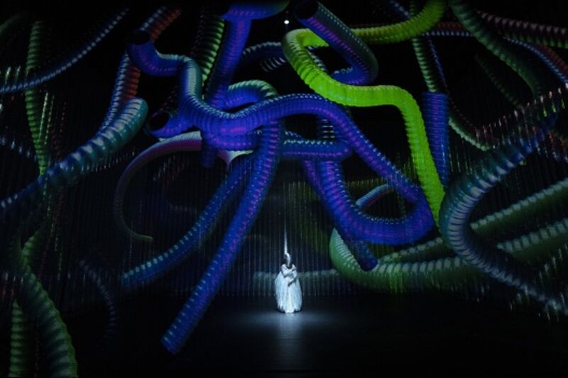 A dancer in the centre, a bright white light on them, with projections of colourful tubes surrounding them