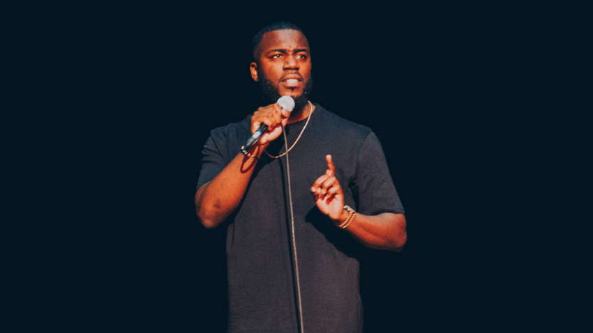 man talking into a microphone with a black shirt on is situated within a dark setting