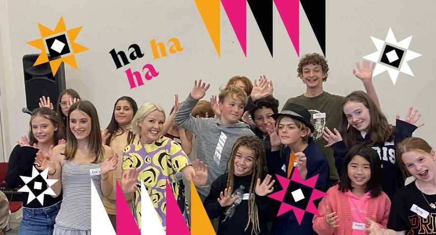 A group of children and one adult female stand smiling with their arms in the air