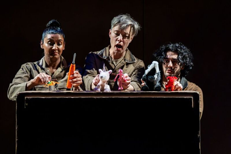Three people kneeling in a dimly lit room, holding up multiple toys. One person looks concerned, one looks angry and one has an expressionless face