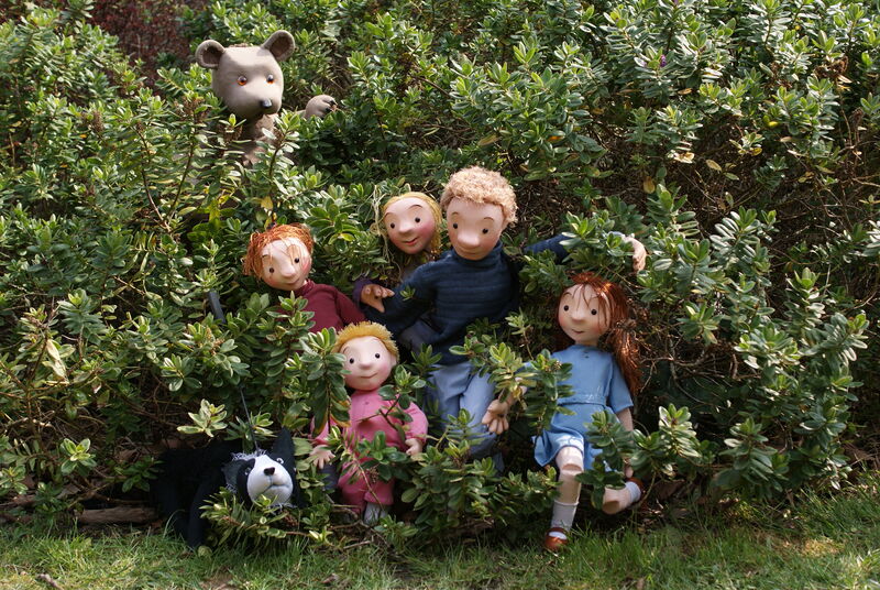 Four wooden puppets of children, their father and a dog running away from a wooden bear puppet through bushes