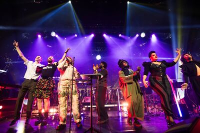 Group of people on stage singing. There are purple and blue lights