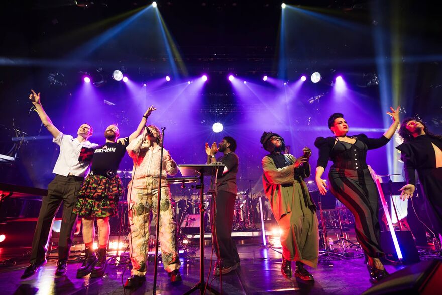 Group of people on stage singing. There are purple and blue lights