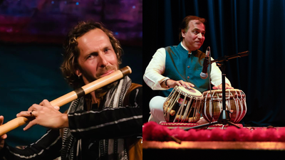 Sanju Sahai playing hand drums whilst sitting down and Jason Kalidas a percussion instrument