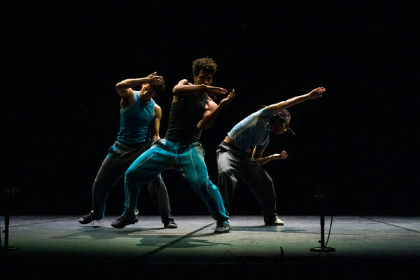 Three dancers dressed in teal athleticwear lean to the right