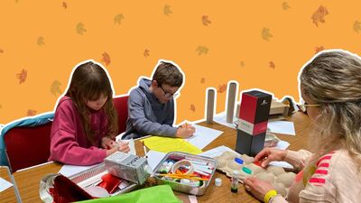 Two kids and an adult drawing and painting on table which has lots of crafting supplies. The image is over a yellow background with autumn leaves