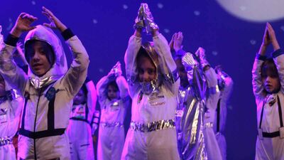 Children on stage dressed as astronauts  with their hands raised above their heads