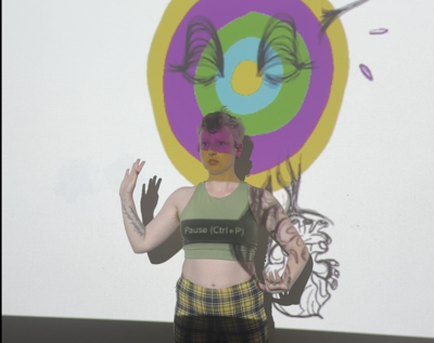 A performer stands in front of a projection screen. They interact with what is being projected