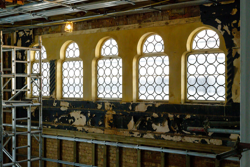5 arched windows with circles in them sit against a wall that is being repaired