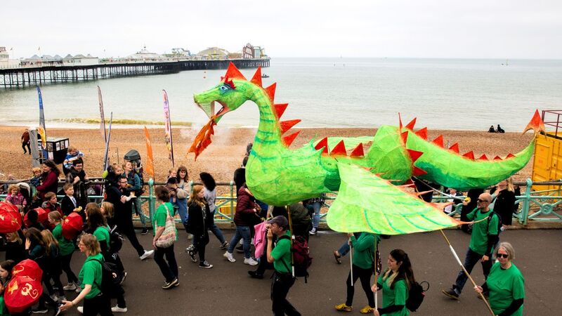 A giant papier mache model of a dragon is paraded along Brighton seafront, Brighton Beach and Pier is visible in the background