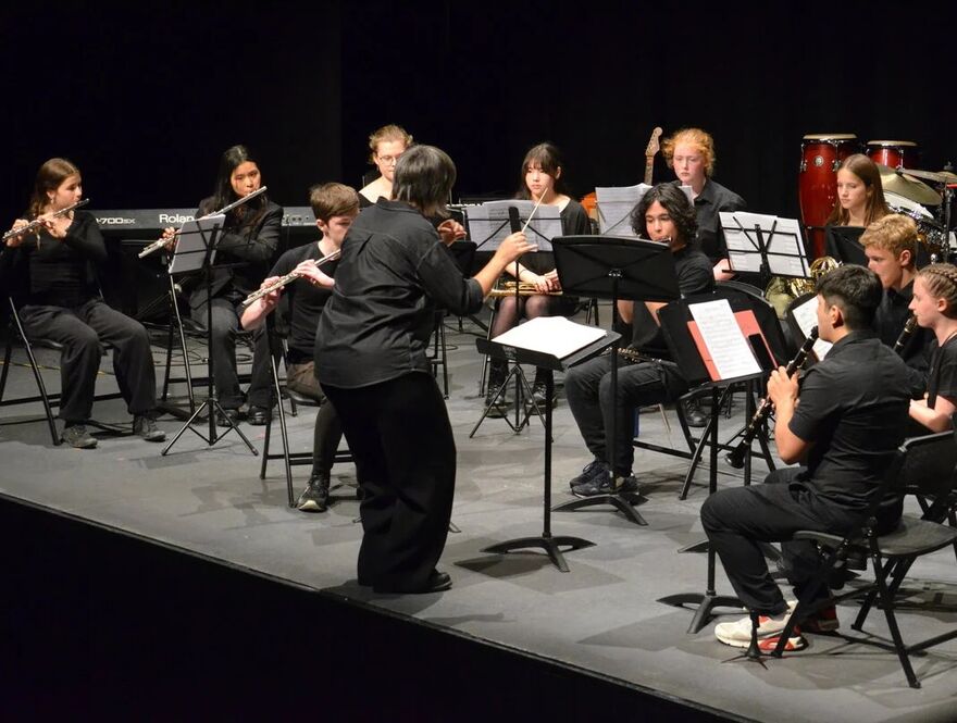 A group of children playing a variety of instruments on stage being conducted