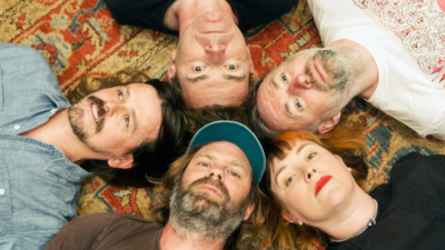 five people lay on a carpet with all of their heads touching one another