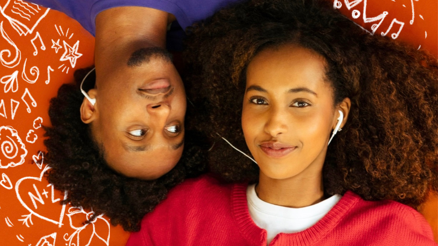 Two people with curly hair lie head-to-head on a bright orange background, sharing white wired earbuds. One person, wearing a purple shirt, looks sideways at the other, who wears a red sweater over a white shirt and smiles softly at the camera. White doodles of musical notes, stars, hearts, and swirls surround them, creating a playful, music-themed scene.