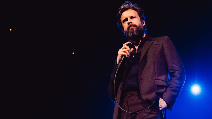 Image of Father John Misty on stage holding a microphone