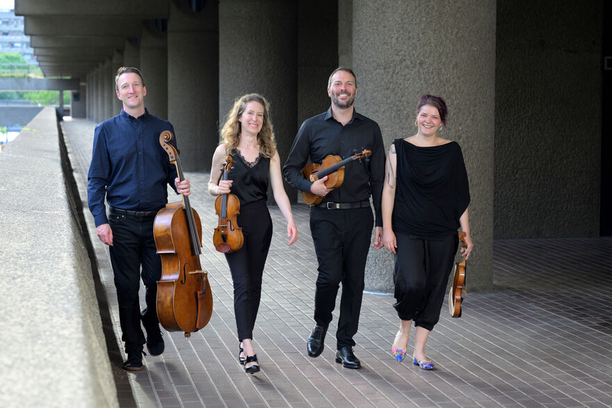 Four people in black outfits walking and holding string instruments