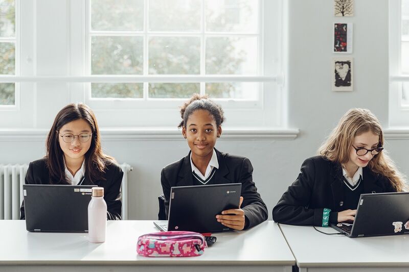 Three secondary school children sitting at desks with their laptops open