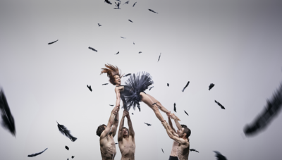 Four shirtless men hold aloft a women dressed as the 'black swan'