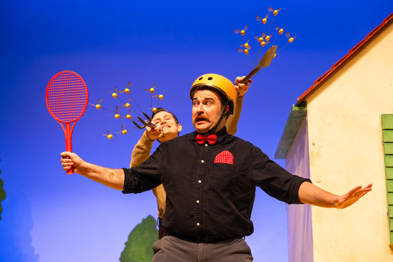 A man wearing a yellow helmet and holding a red racket looks frightened as bees fly towards him from behind