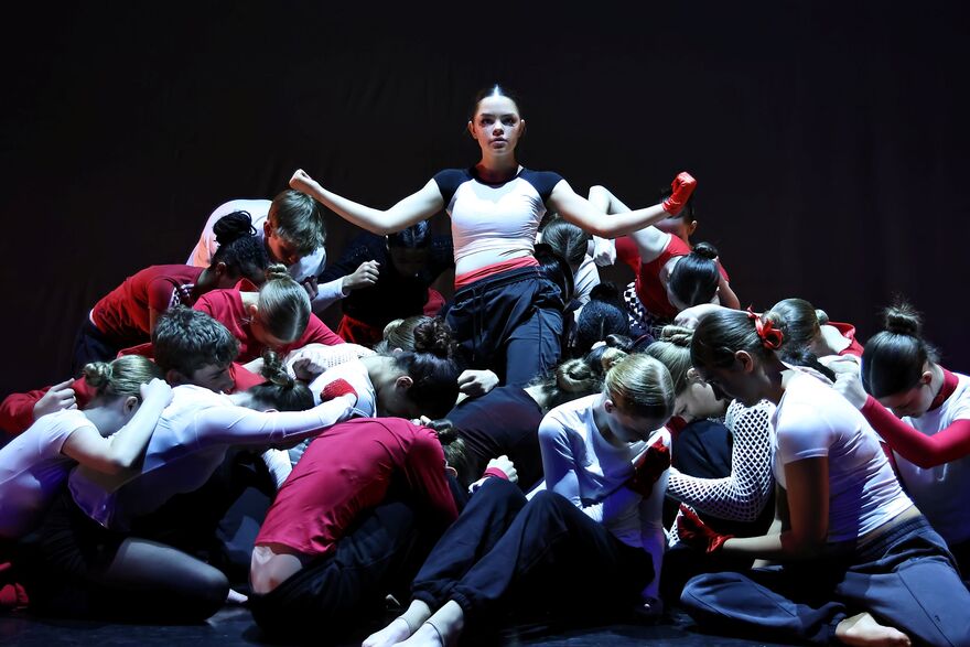 A group of dancers on a stage. There is one girl above them holding her fists up