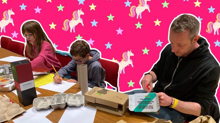 A man and two children crafting. The background is pink with blue, green, pink and yellow stars and cream unicorns