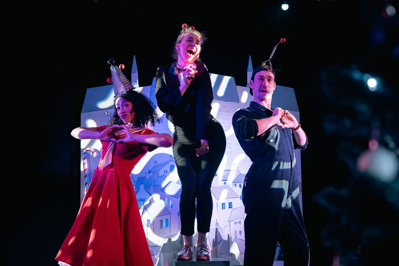 A man and woman hold their hands to their chest in a heart shape with a woman singing inbetween them