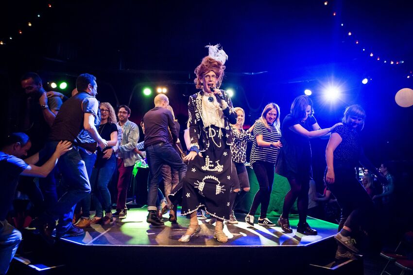 Ida Barr sings on stage surrounded by people doing the conga