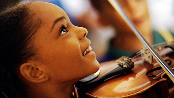 A smiling girl plays the violin in a music lesson