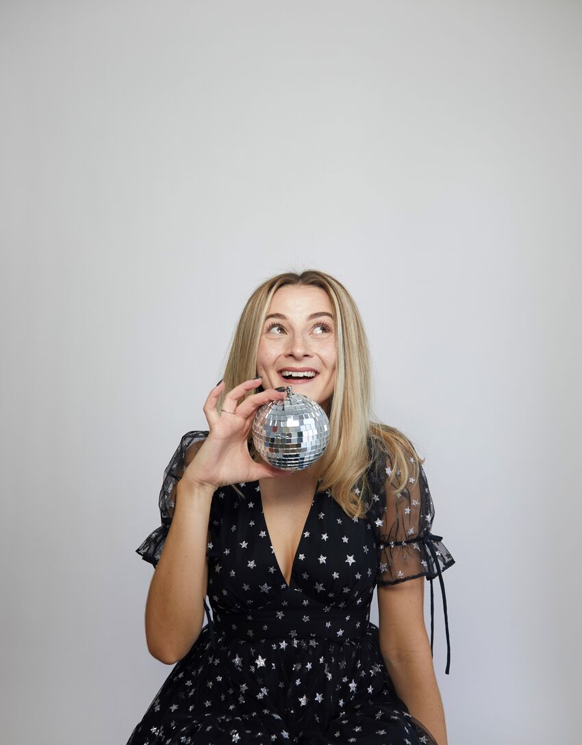 Hannah sitting in a black star dress holding a disco ball