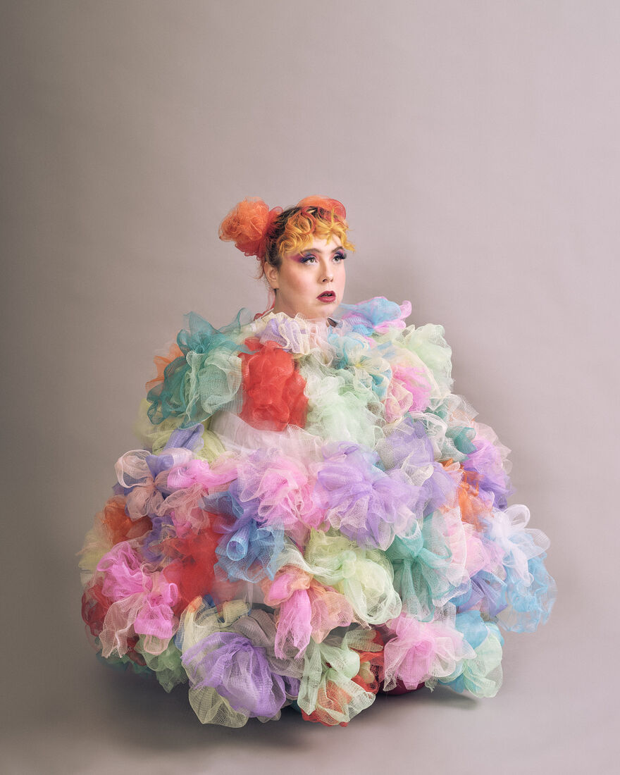 Someone with their hair in two orange space buns, crouching wearing multi-coloured tulle outfit