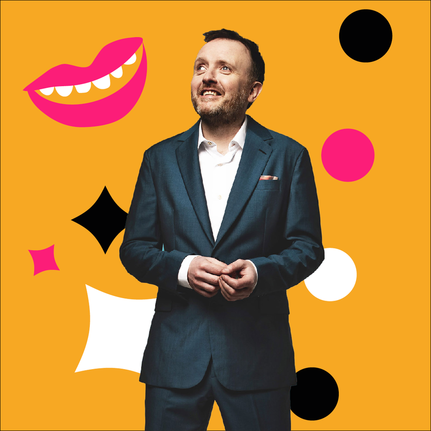 Chris McCausland standing in front of a yellow backgroun in a suit