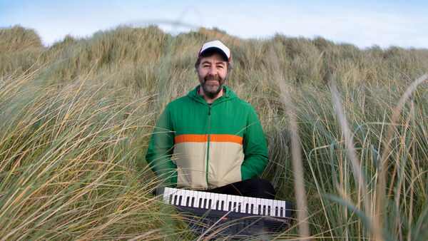David O'Doherty in a field of long grass with a tiny piano