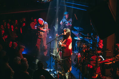 Four members of HEJIRA standing on stage under a red light perfoming to a crowd