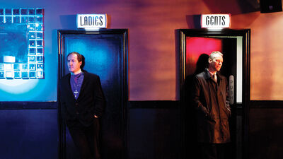 On the left, a priest stands in front of a door to the ladies, a man in a trenchcoat stands in front of a door to the gents on the right