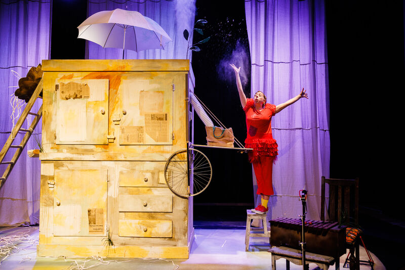 A woman dressed as a red hen stands on a stool and throws flour into the air