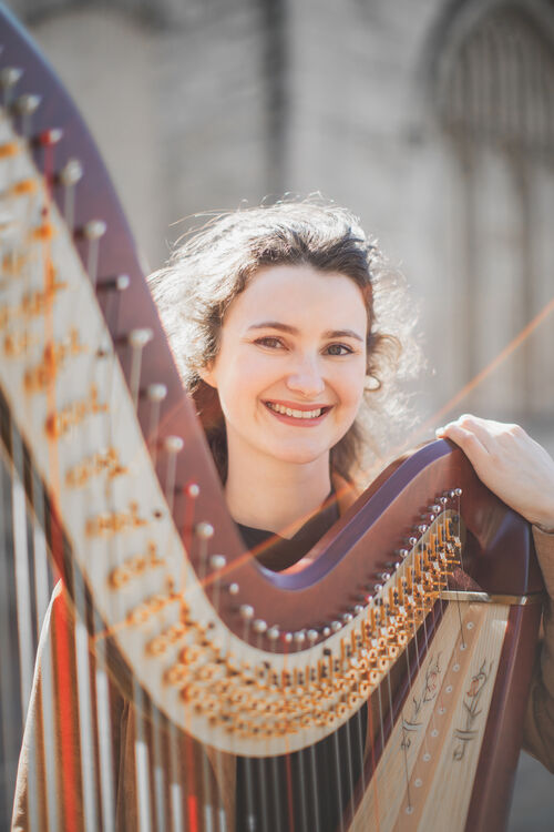 A young white woman smiles widely while holding a harp in front of her