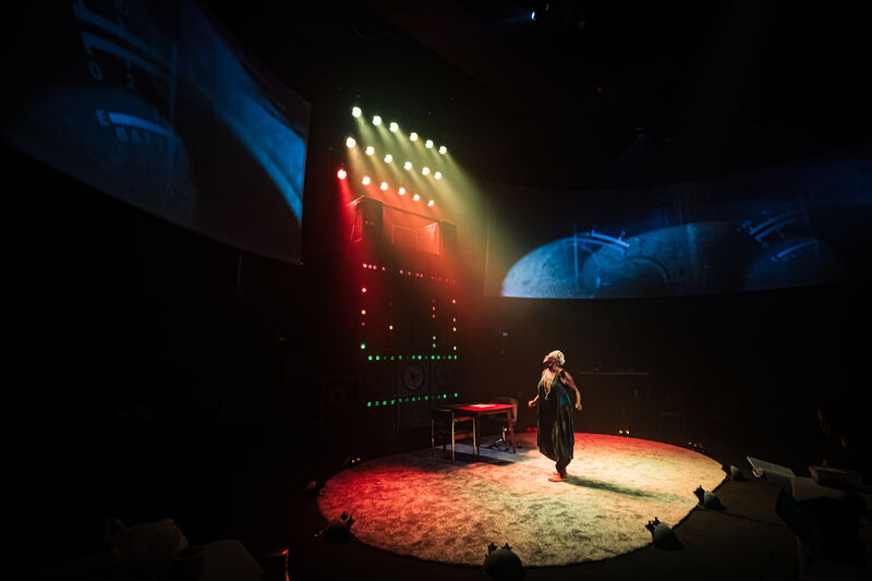 Sutara Gayle on stage lit from above by red and yellow light which casts a warm oval of light over the stage