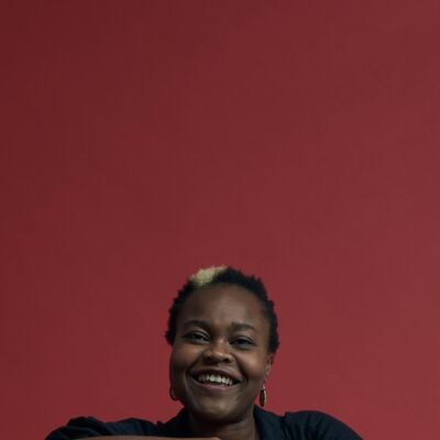 Tendai, a black women with short black hair and a bleached streak through it, smiles widely