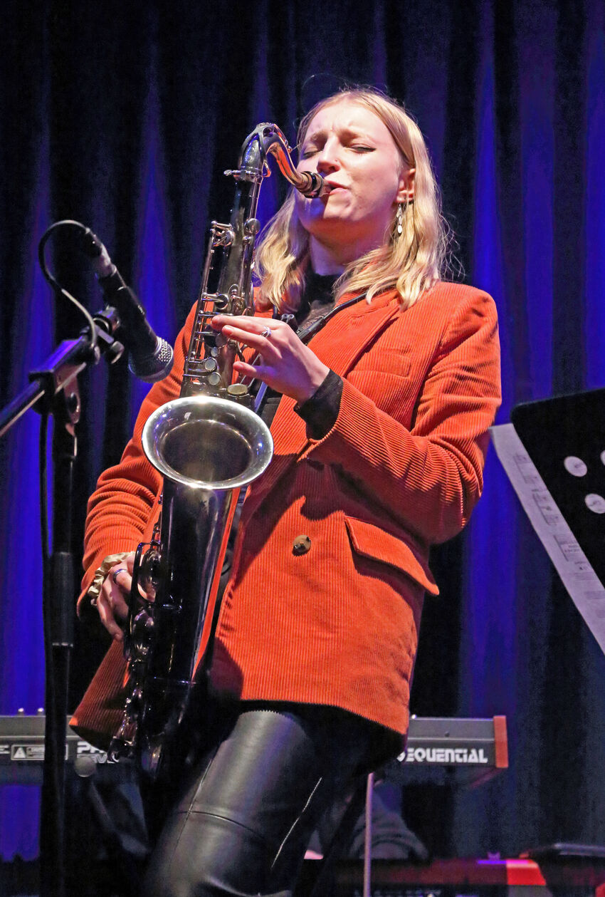 Emma Rawicz wearing a red jacket and playing a saxaphone
