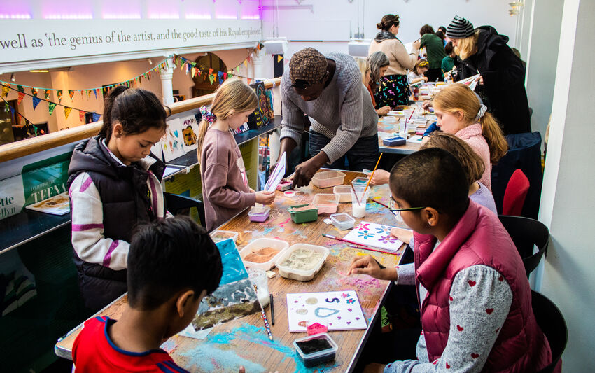 multiple people sit on a table and work on arts and crafts