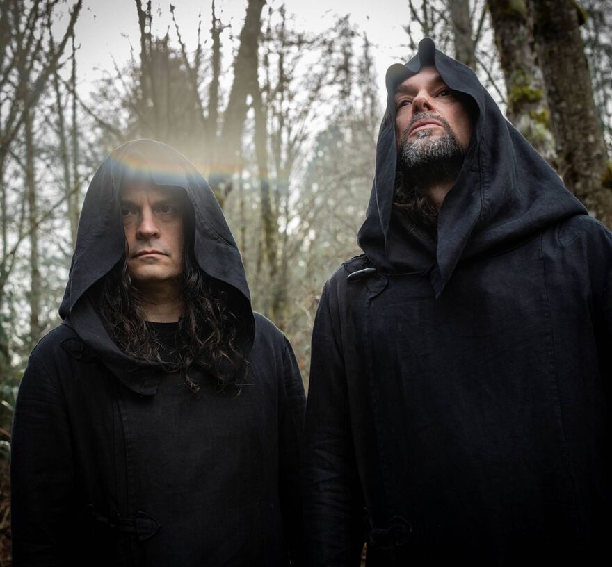 Two men in a forest wearing black capes