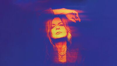 A woman with long hair poses against a deep blue background, one arm raised above her head. The image uses a vivid blue, magenta, and orange color treatment.