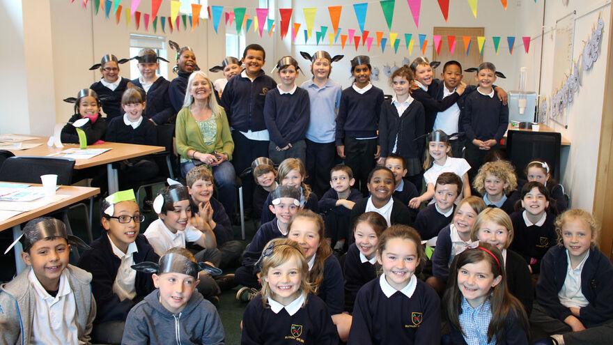 A class of children sit with an author facing the camera below colourful bunting