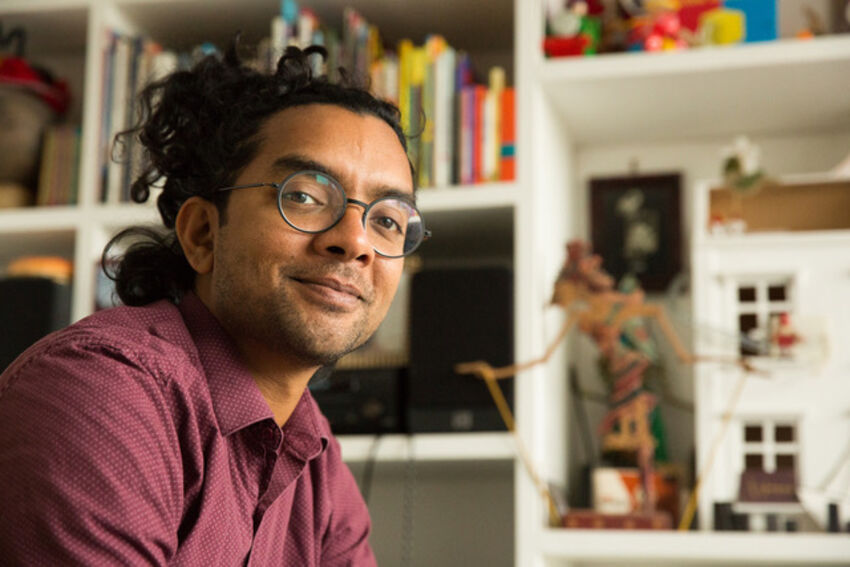 a man with rounded glasses and a red shirt smiles
