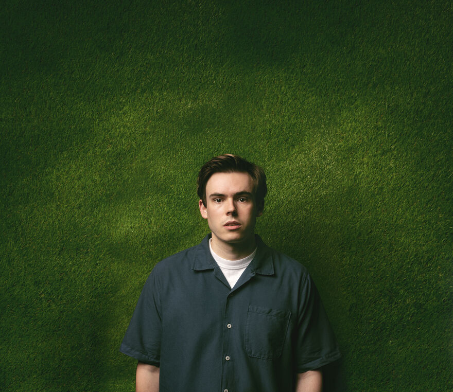 man looks directly forward in a navy blue shirt in front of a green background
